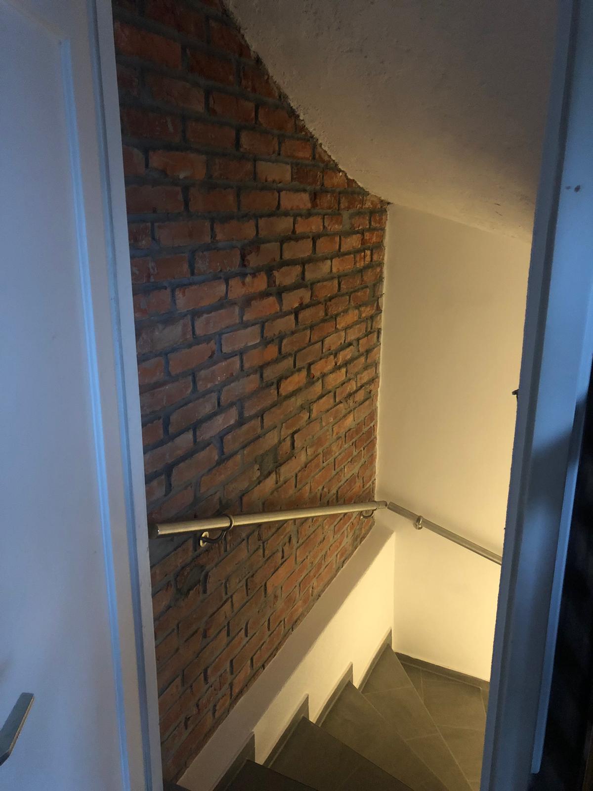 Sanierter Treppenabgang mit freigelegter Sichtziegelwand und neuem Handlauf.